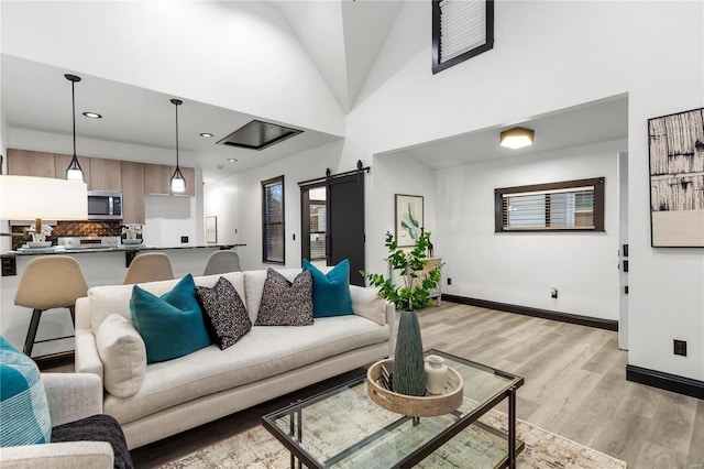 living area featuring recessed lighting, light wood-style flooring, a high ceiling, a barn door, and baseboards