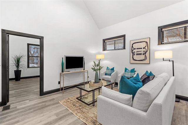 living area featuring high vaulted ceiling, visible vents, light wood-style flooring, and baseboards