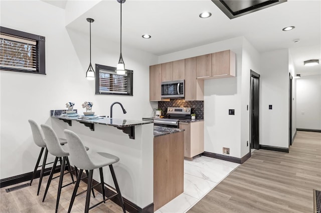 kitchen featuring a breakfast bar area, decorative backsplash, appliances with stainless steel finishes, a peninsula, and baseboards