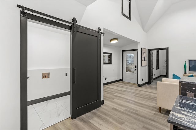 interior space with light wood-type flooring, high vaulted ceiling, a barn door, and baseboards