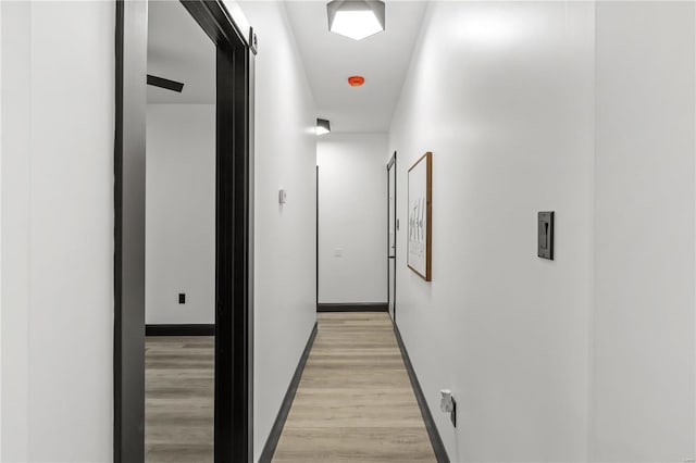 corridor featuring light wood finished floors and baseboards