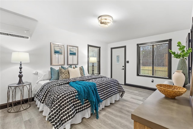 bedroom featuring light wood-type flooring, an AC wall unit, and baseboards