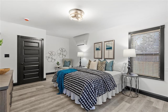 bedroom featuring light wood-type flooring, a wall mounted air conditioner, and baseboards