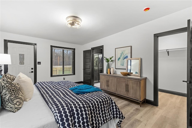 bedroom with a spacious closet, a closet, light wood-style flooring, and baseboards