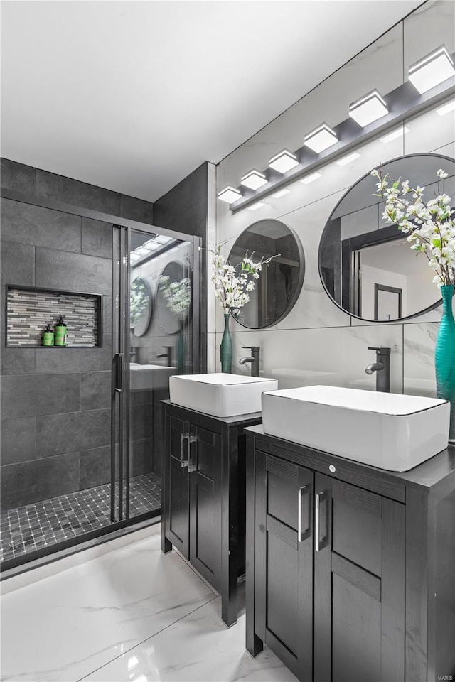 bathroom featuring marble finish floor, a stall shower, two vanities, and a sink