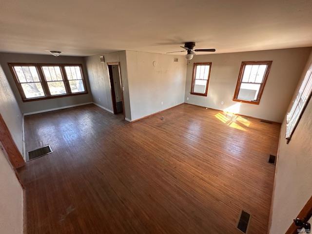 unfurnished living room with baseboards, dark wood-style flooring, visible vents, and a ceiling fan