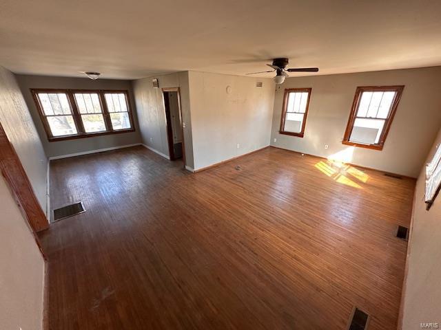 unfurnished living room featuring a ceiling fan, baseboards, visible vents, and dark wood-type flooring