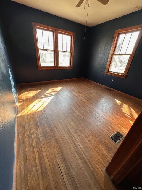 spare room featuring a healthy amount of sunlight, wood-type flooring, visible vents, and ceiling fan