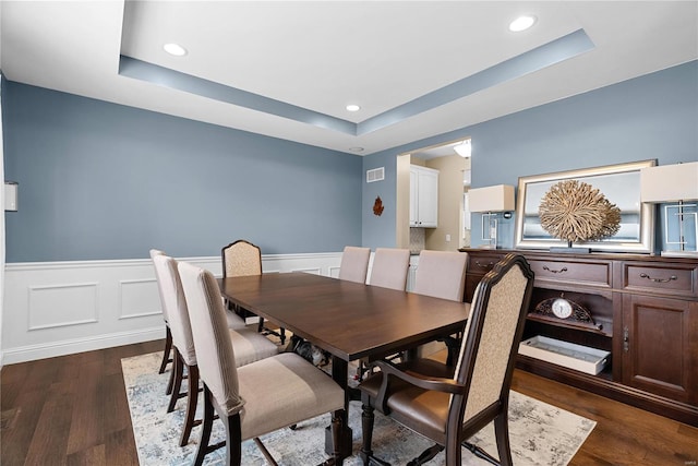 dining space featuring a raised ceiling, visible vents, dark wood-style floors, and a wainscoted wall