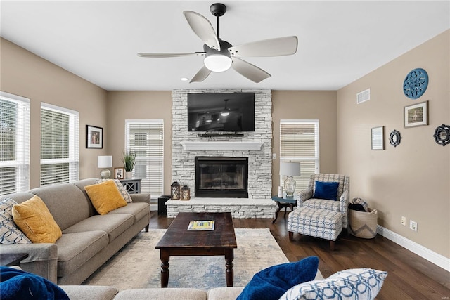 living area with visible vents, dark wood finished floors, baseboards, a stone fireplace, and ceiling fan