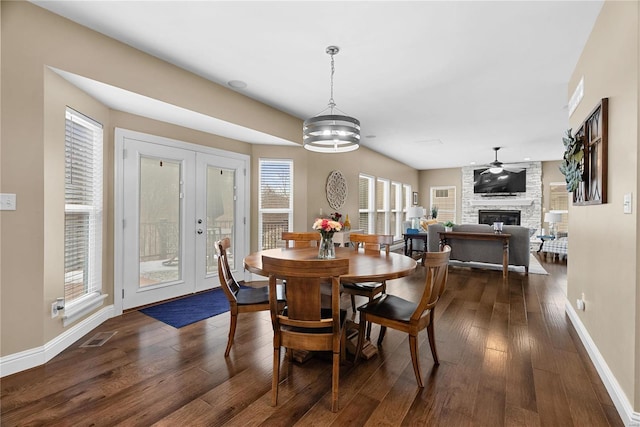 dining area featuring visible vents, dark wood finished floors, baseboards, a stone fireplace, and a notable chandelier