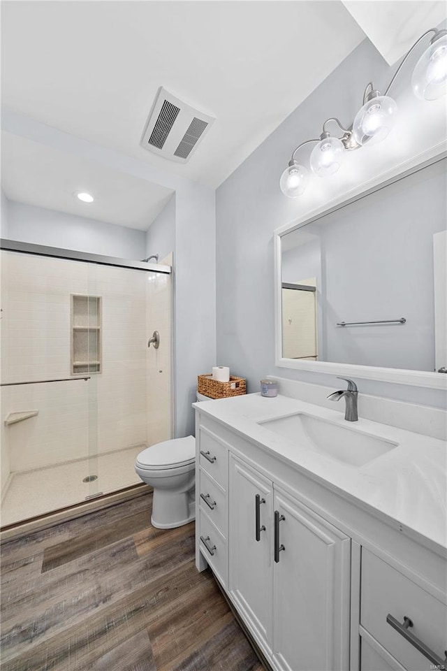 full bath featuring toilet, wood finished floors, vanity, visible vents, and a stall shower