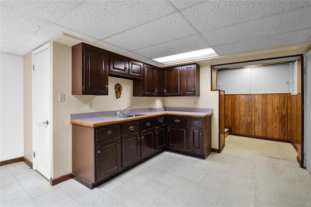 kitchen featuring sink, a paneled ceiling, wooden walls, and dark brown cabinetry