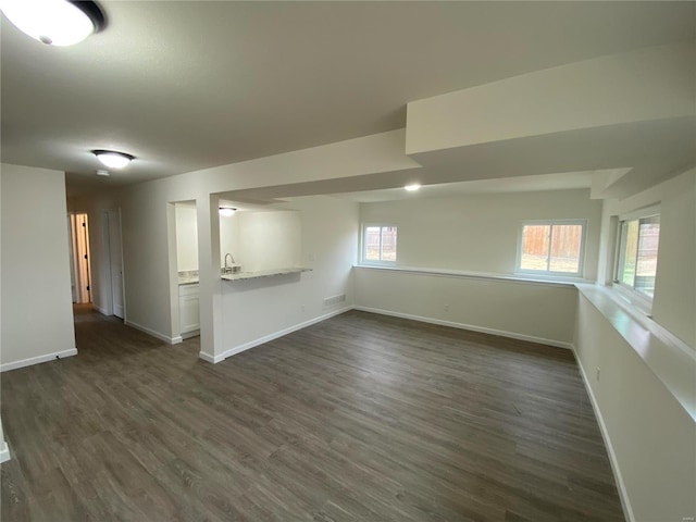 basement featuring a sink, dark wood finished floors, visible vents, and baseboards