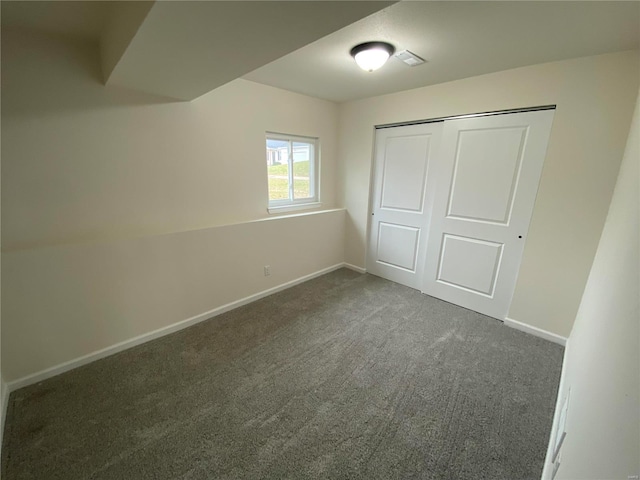 unfurnished bedroom featuring baseboards, dark colored carpet, and a closet