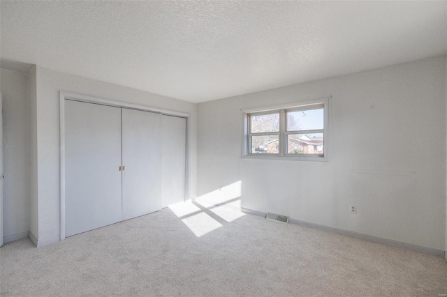 unfurnished bedroom featuring carpet floors, a closet, visible vents, and a textured ceiling