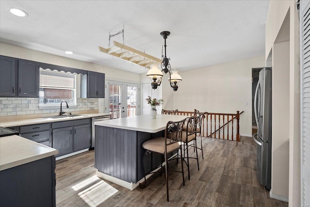 kitchen featuring appliances with stainless steel finishes, a center island, hanging light fixtures, light countertops, and a sink