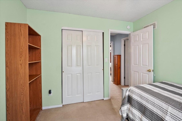 bedroom with a textured ceiling, light colored carpet, visible vents, baseboards, and a closet