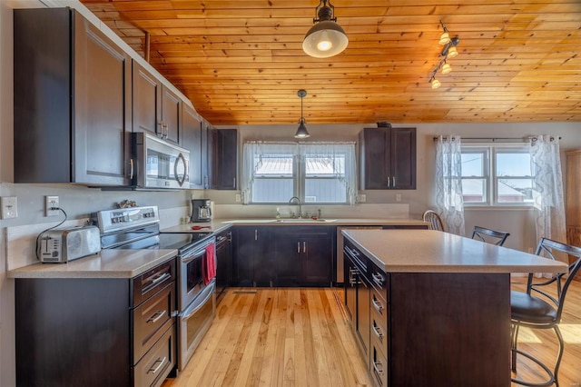 kitchen with dark brown cabinets, hanging light fixtures, stainless steel appliances, sink, and a kitchen bar