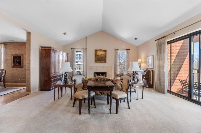 dining area with visible vents, light colored carpet, a warm lit fireplace, and lofted ceiling