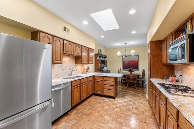 kitchen featuring visible vents, a peninsula, a sink, stainless steel appliances, and a chandelier