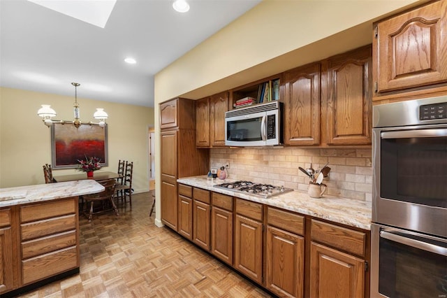 kitchen with backsplash, light stone countertops, decorative light fixtures, appliances with stainless steel finishes, and brown cabinetry