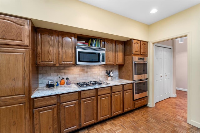 kitchen with backsplash, baseboards, light stone counters, brown cabinets, and appliances with stainless steel finishes