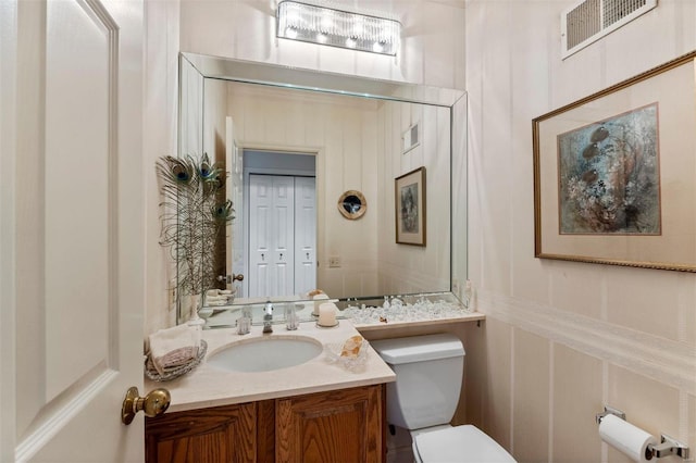 half bath featuring visible vents, vanity, toilet, and a decorative wall