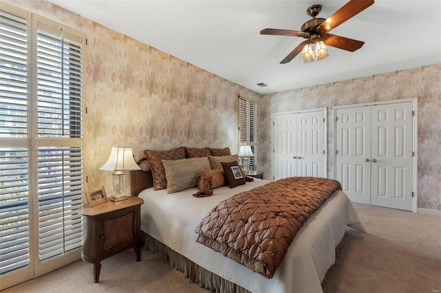 bedroom featuring visible vents, multiple closets, carpet floors, wallpapered walls, and ceiling fan