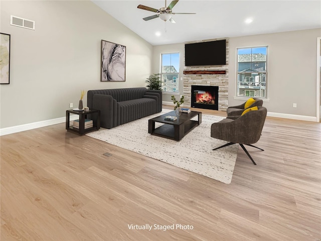 living room with light hardwood / wood-style flooring, ceiling fan, vaulted ceiling, and a fireplace