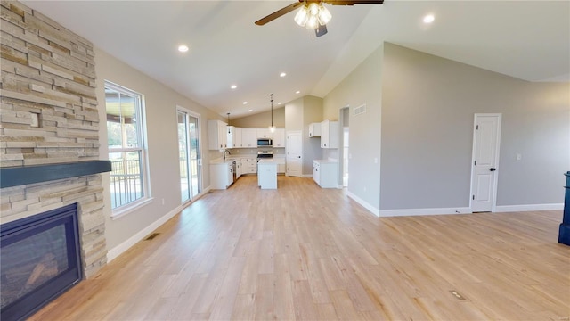 unfurnished living room with sink, light wood-type flooring, ceiling fan, a fireplace, and high vaulted ceiling