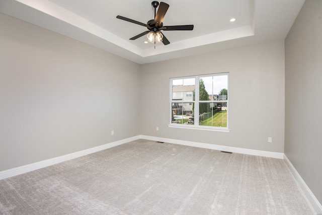 carpeted spare room with a tray ceiling and ceiling fan