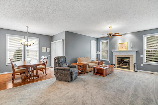 living area with light colored carpet, a textured ceiling, a tile fireplace, baseboards, and ceiling fan with notable chandelier