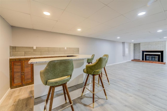 bar with recessed lighting, baseboards, a brick fireplace, and light wood-style flooring