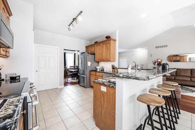 kitchen with stainless steel appliances, dark stone counters, lofted ceiling, a breakfast bar, and light tile patterned floors