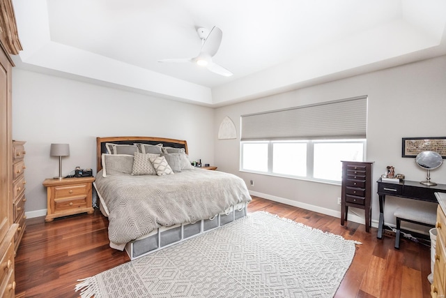 bedroom with dark wood-type flooring, ceiling fan, and a raised ceiling