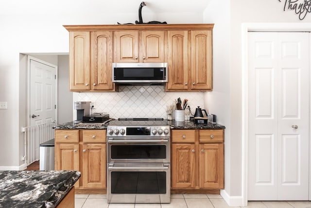 kitchen with dark stone counters, backsplash, stainless steel appliances, and light tile patterned floors