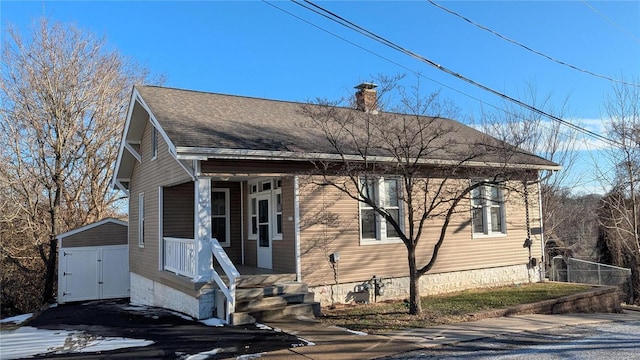 view of front facade featuring roof with shingles, a chimney, a storage shed, fence, and an outdoor structure