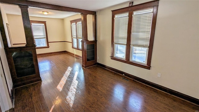 unfurnished living room featuring decorative columns, visible vents, baseboards, and dark wood finished floors