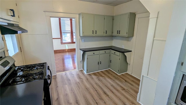 kitchen with gas range oven, dark countertops, light wood-type flooring, under cabinet range hood, and baseboards