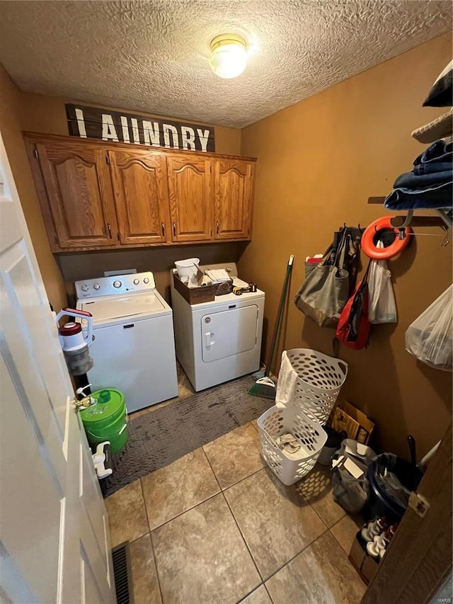 laundry area with light tile patterned flooring, cabinets, a textured ceiling, and washing machine and clothes dryer