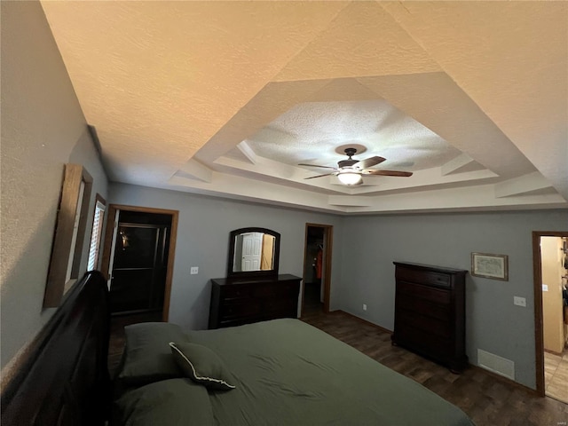 bedroom featuring a tray ceiling, dark wood-type flooring, a textured ceiling, and ceiling fan