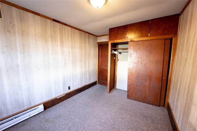 unfurnished bedroom with wood walls, light carpet, baseboard heating, ornamental molding, and a closet