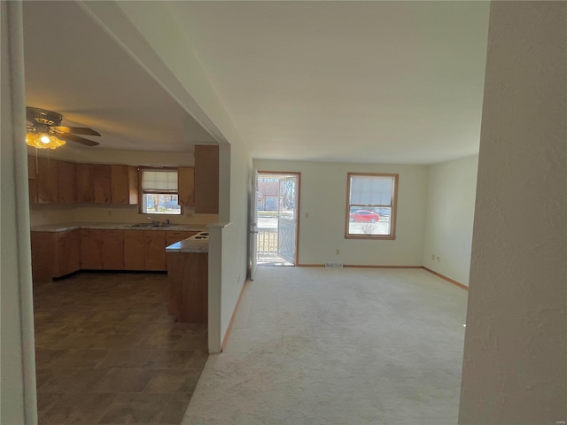 kitchen featuring light carpet, a sink, a ceiling fan, baseboards, and light countertops