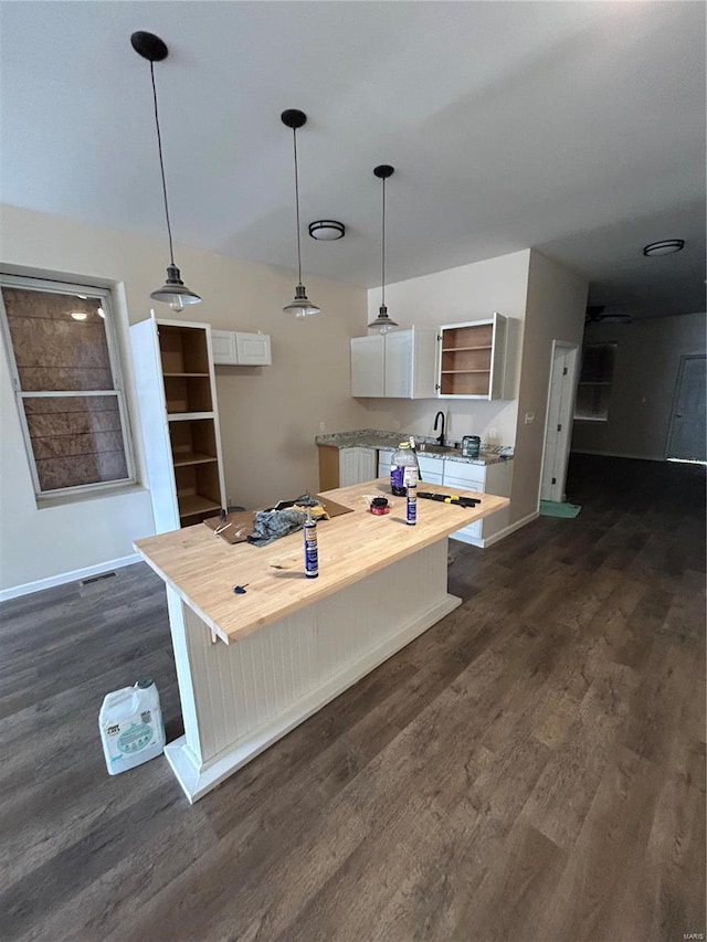 kitchen featuring dark wood-style flooring, a breakfast bar area, open shelves, hanging light fixtures, and white cabinets