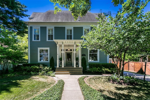 view of front of house with a front lawn, a shingled roof, and fence