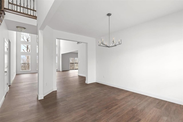 unfurnished dining area featuring a notable chandelier, dark wood-type flooring, and a towering ceiling