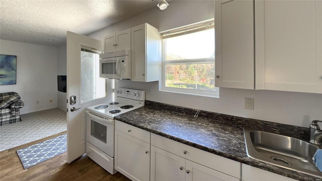 kitchen featuring white appliances, white cabinets, a sink, and a textured ceiling