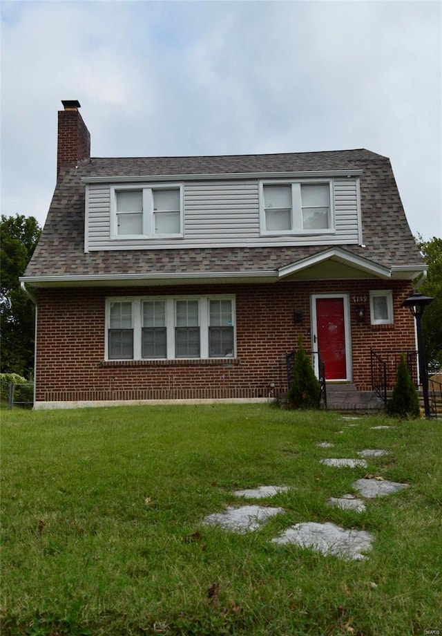 view of front of property featuring brick siding, a chimney, a front yard, and a shingled roof