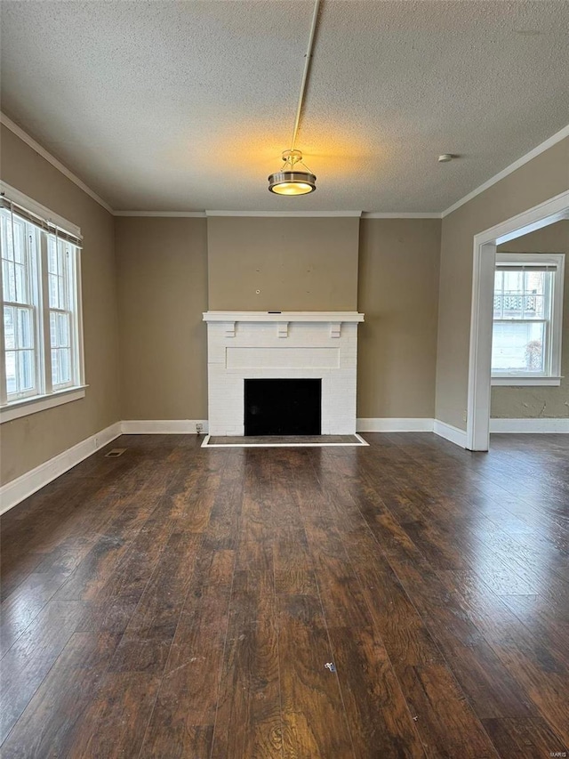 unfurnished living room with dark wood-type flooring, a brick fireplace, crown molding, and a healthy amount of sunlight